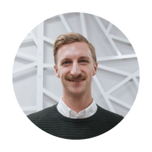 Daniel Rempel smiles at the camera in front of a white geometric-patterned wall.